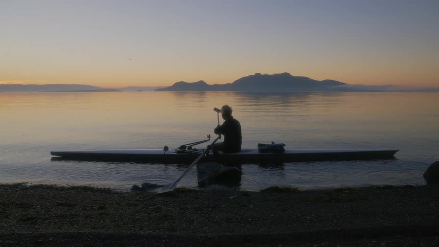 Man assembling the paddles on a canoe floating on the coast of a lake next to the mountains at evening