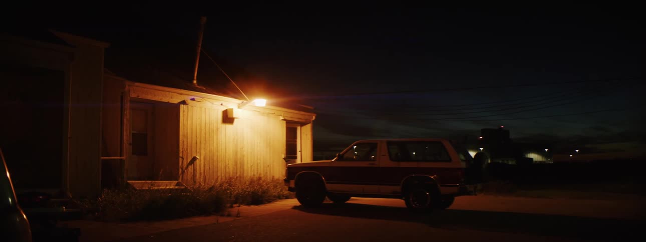 Pickup truck parked in front of a house under a single lamp in the countryside at night