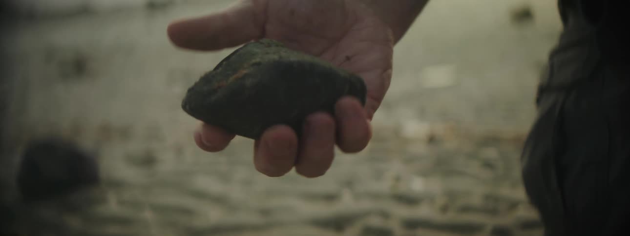 A man picking up a stone from sandy ground
