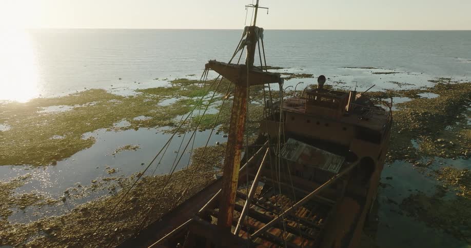 Sun glares off water on coast near wreck of large sailing ship