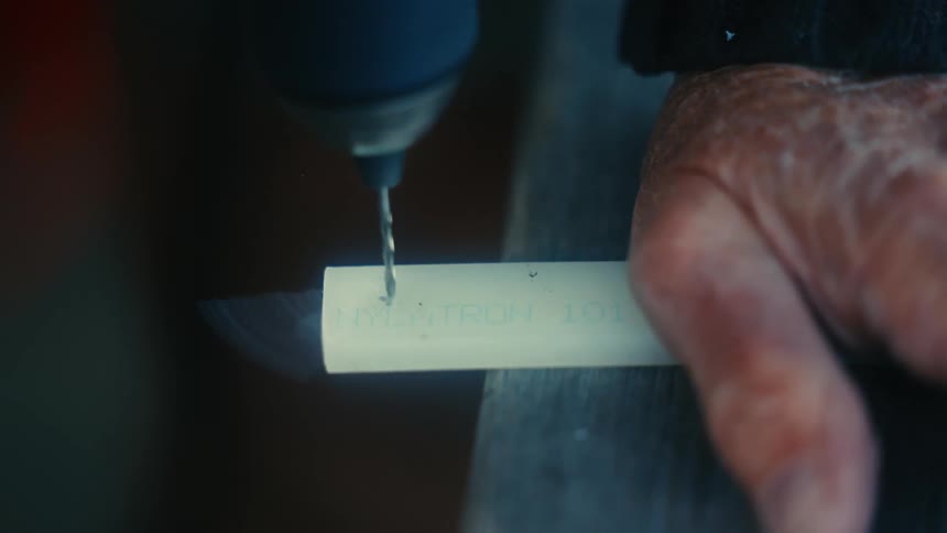 A man is drilling in a piece of wood outdoors