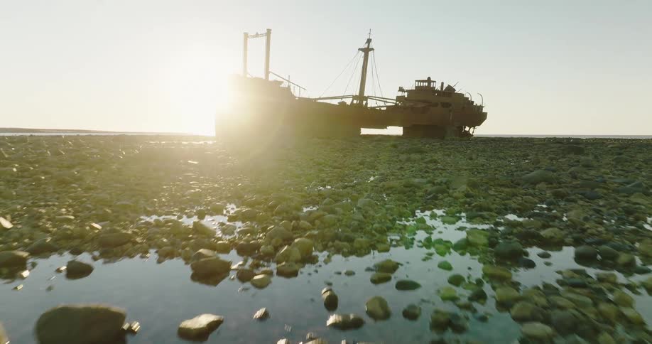 Aerial view of sunlight shining through a rusted shipwreck on the surface of a marsh at evening
