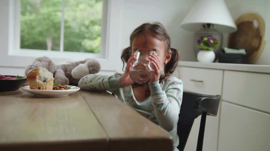 Young girl wearing pajamas sitting at the table drinking a big glass of water