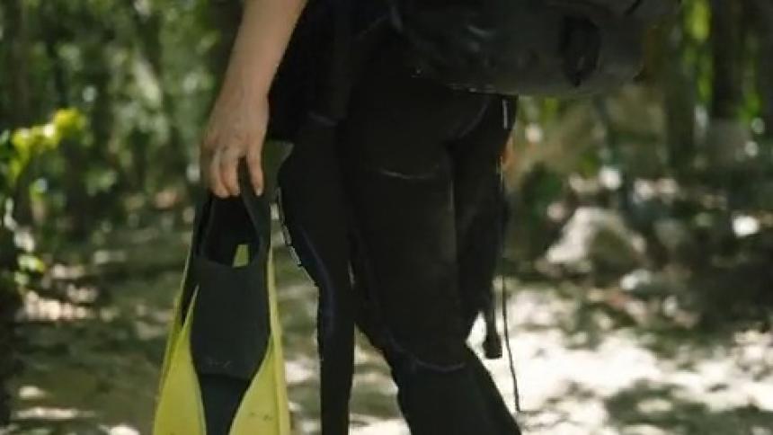 A young woman carry dive fins hikes through the jungle