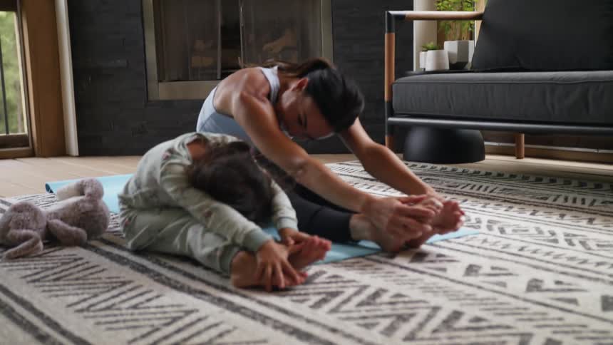 A woman is sitting on the floor doing exercises with her little girl
