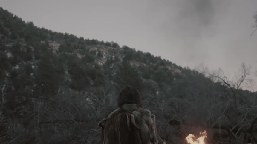 A man stands with a torch before a hill