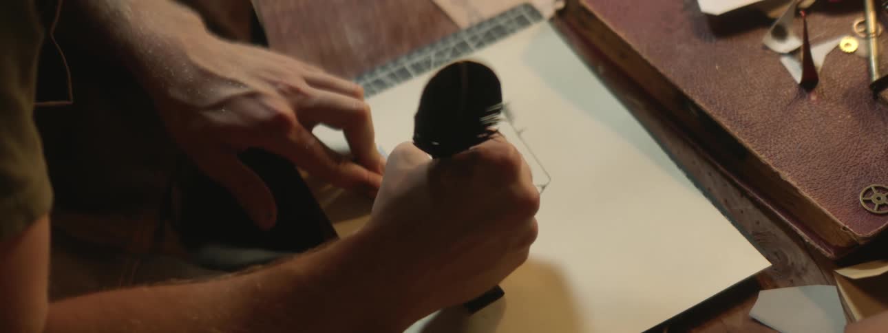 Close up of a man drawing with a feather and ink on paper using a ruler
