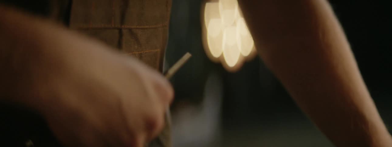 Man working on a dimly lit workshop takes a small scissor hanging from his apron