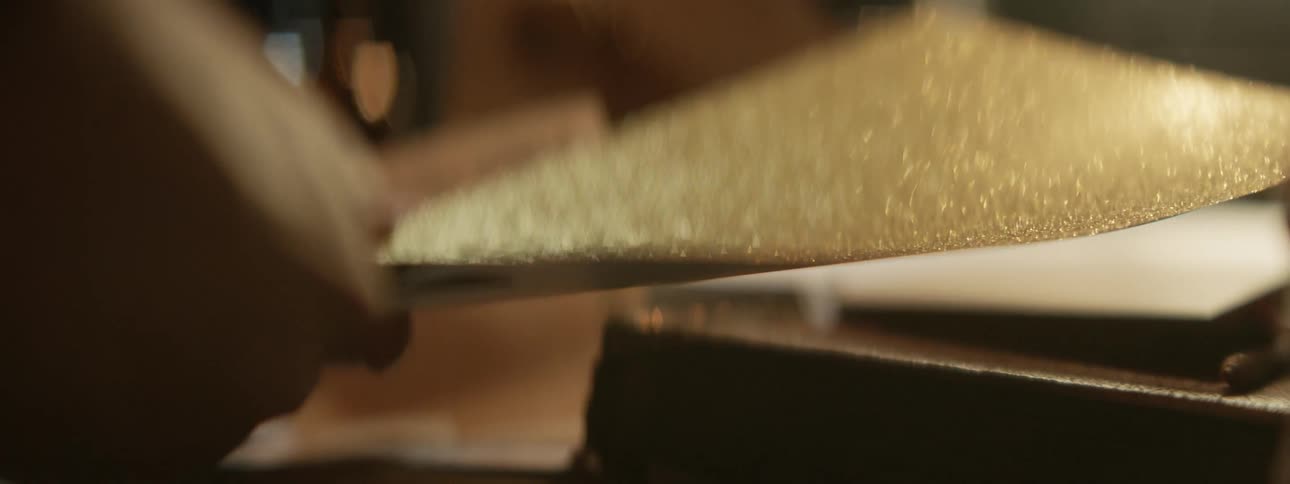 Someone is sitting at a table cutting gold glitter paper with scissors and it sparkles as it moves