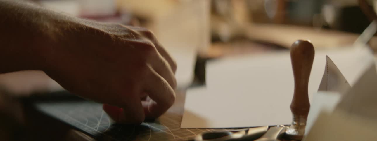 Close up of the hands of a man cutting and folding pieces of paper on a desk at home