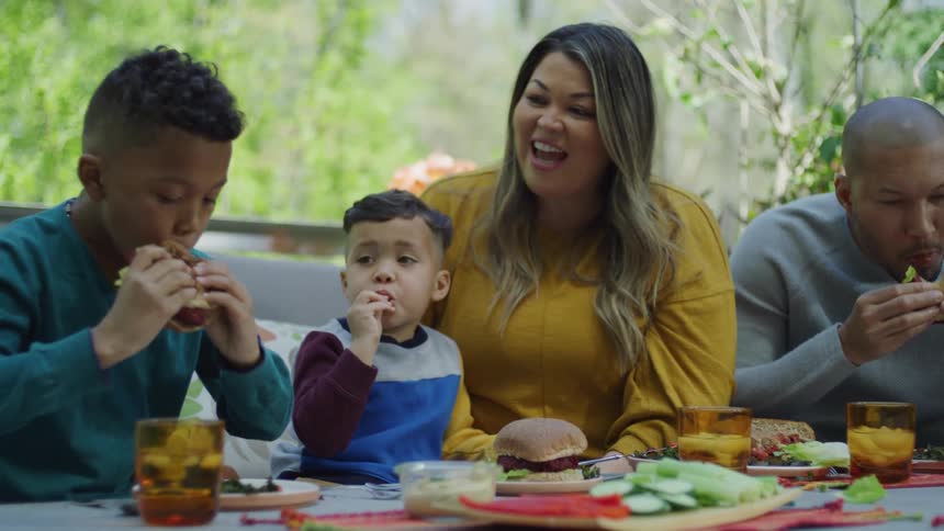 Family sits outdoors eating burgers
