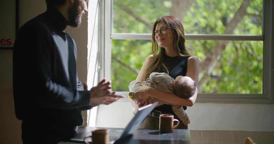 A man types on the laptop as a woman rocks her baby