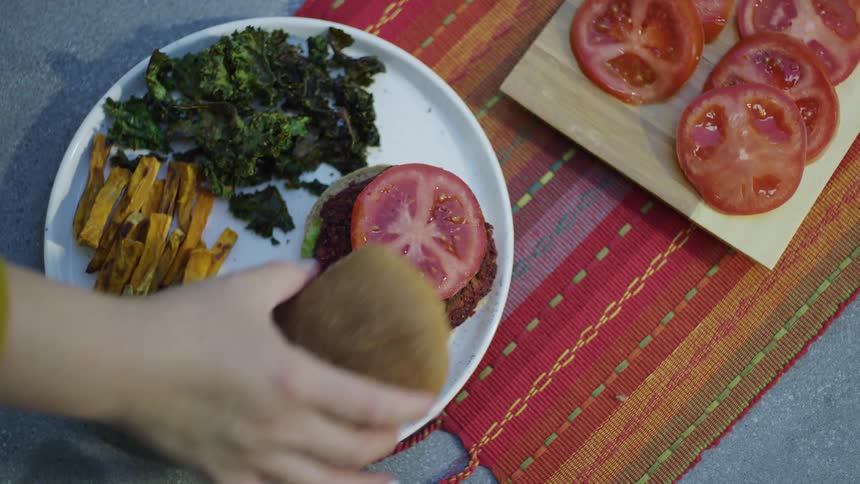 A person puts a tomato on the burger and picks up the dish