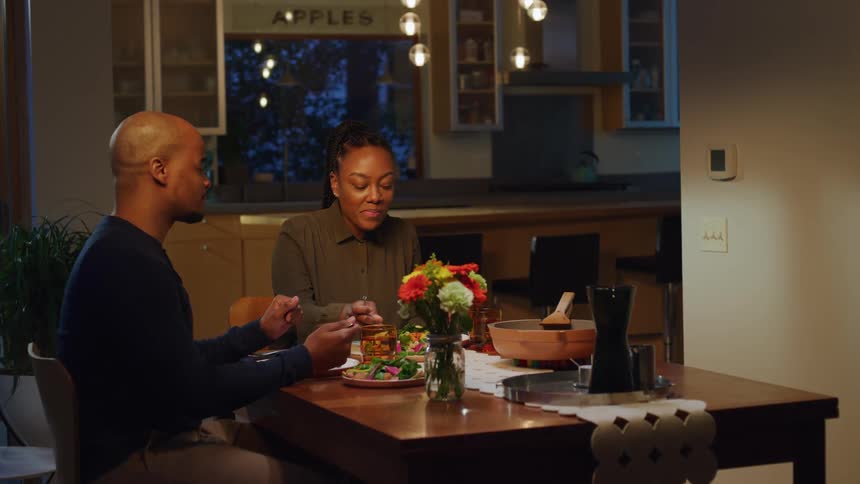 Couple sit at dining table at night talking and eating