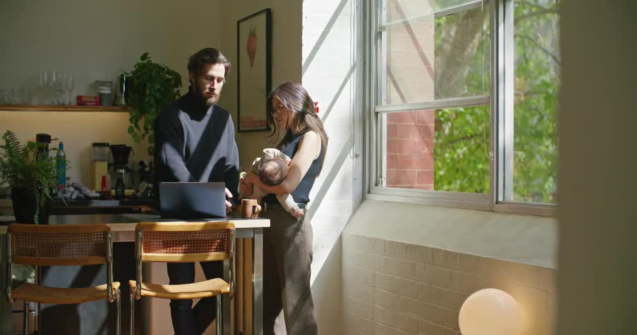 Mother holds baby as she and father talk over contents on laptop
