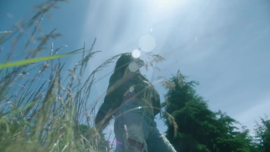 Young woman wearing a jacket and jeans looks at the sky on the countryside