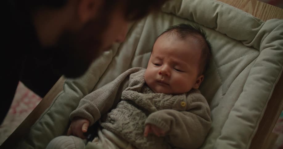 Bearded young man cuddles and talks to his newborn baby at home