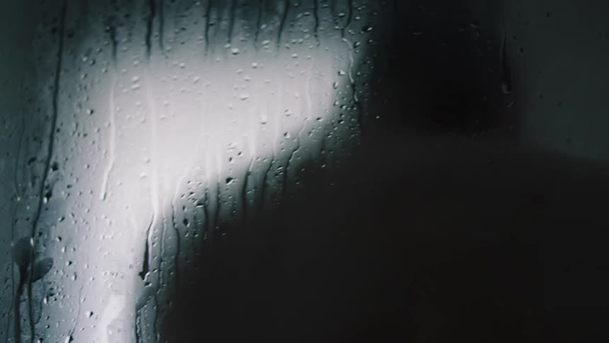 Blurred silhouette of a person taking a shower behind a wet fogged glass