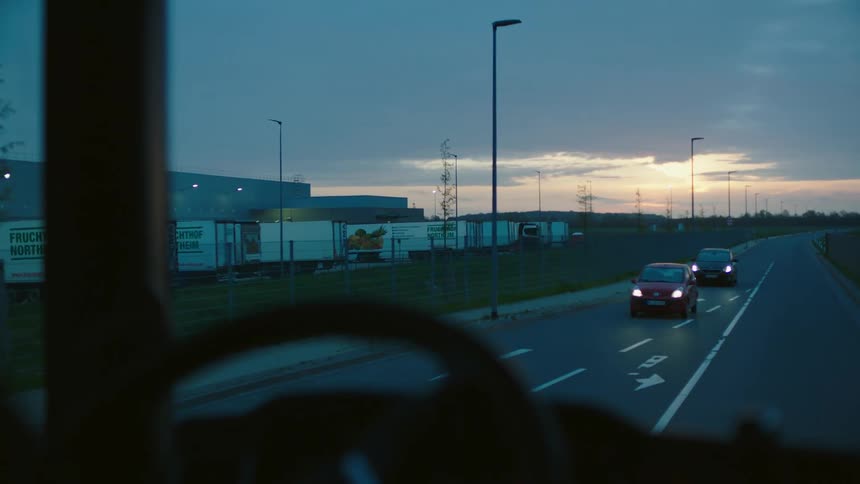 Highway runs past warehouse and toward red horizon before curving
