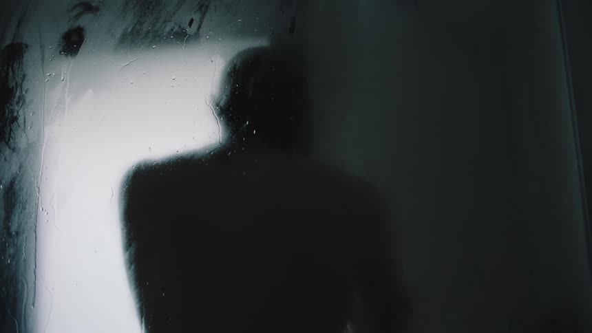 The silhouette of a man showering behind a steam fogged glass door