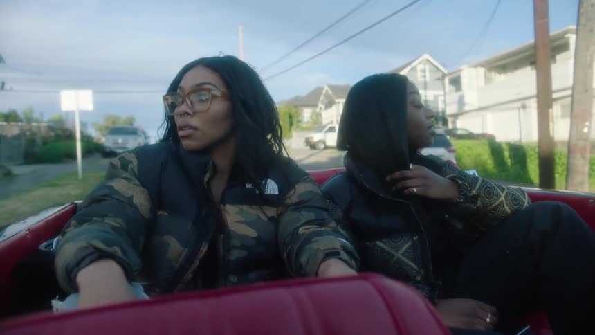 Two young beautiful woman wearing thick jackets sitting on the back seat of a convertible driving in the morning