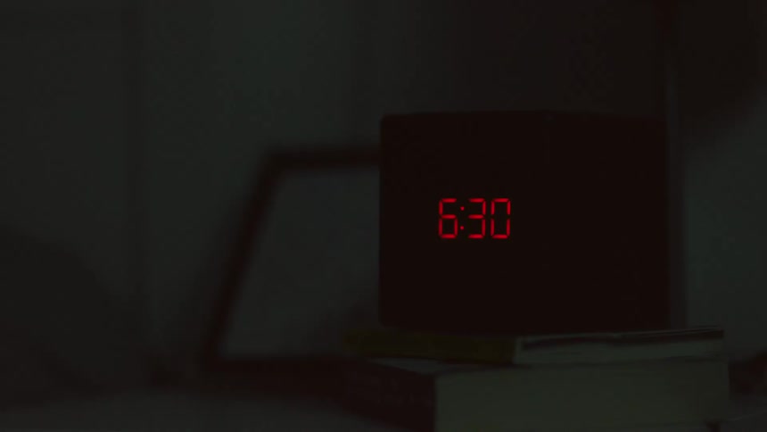 A clock is sitting on top of books on a table flashing the numbers 630 in the darkness