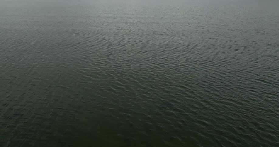 Light shines on the water as it ripples and waves under a cloudy sky with mountains in the distance