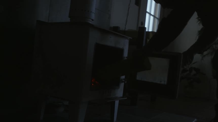 A man stands up and puts a piece of firewood into a small furnace