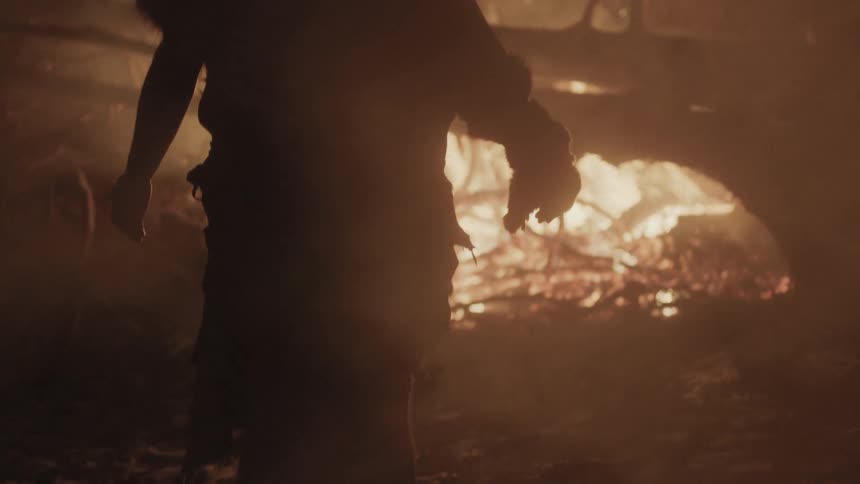 Wilderness man standing in front of a bonfire on a smoky night