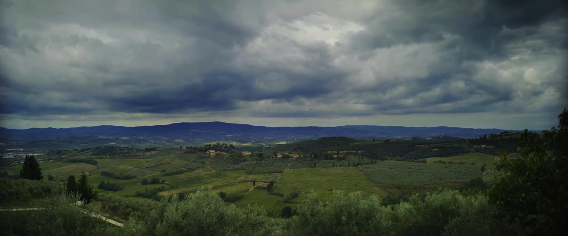 Dark clouds float over green field and distant buildings