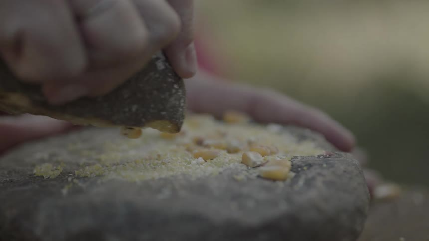 A person is mashing corn on a rock