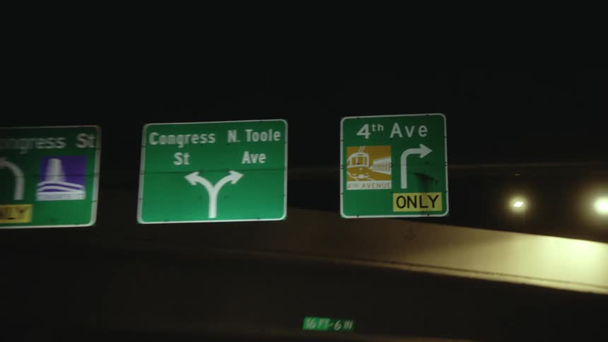 Vehice drives on highway passing under traffic signs at night