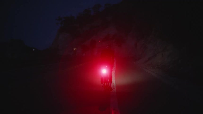 Male cyclist rides bicycle with tail red flashing light on mountain road at night