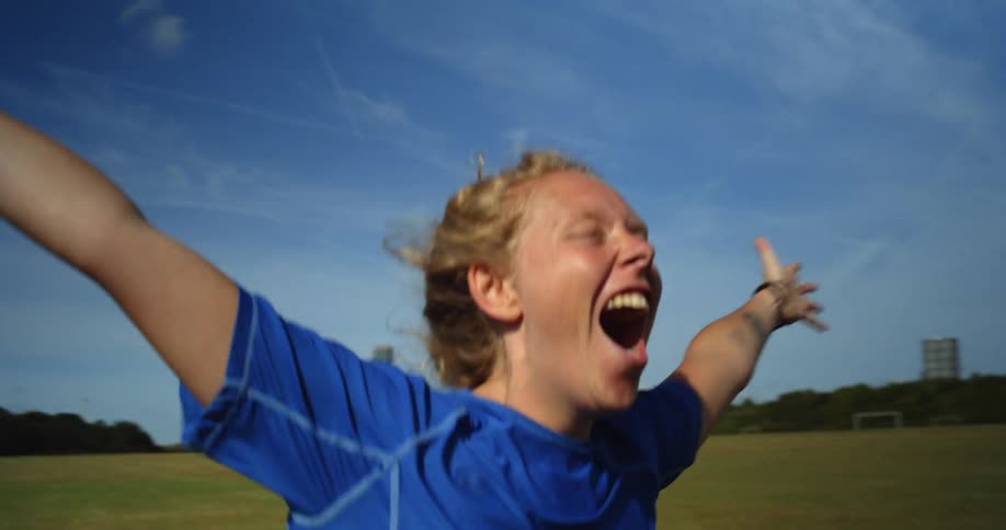 A woman screams with joy on a grass sports field running with arms outstretched
