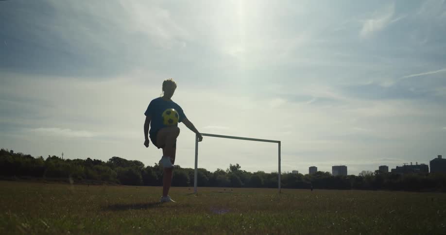 Female athlete partly silhouetted against the sun practices with a soccer ball in a park