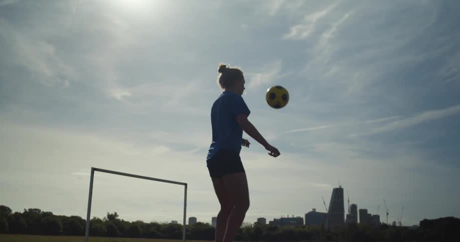 A young woman plays keep-ups with a soccer ball in a recreation ground