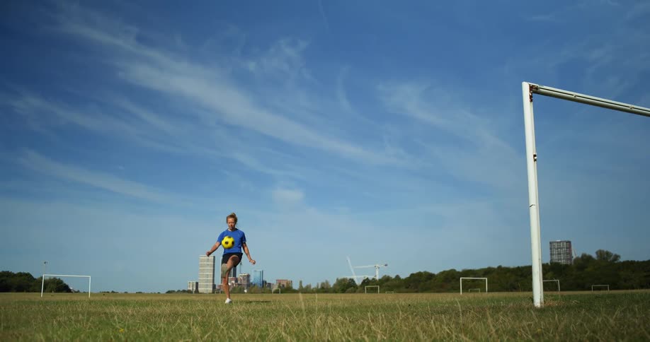 The woman is kicks a soccer ball in a large recreation ground