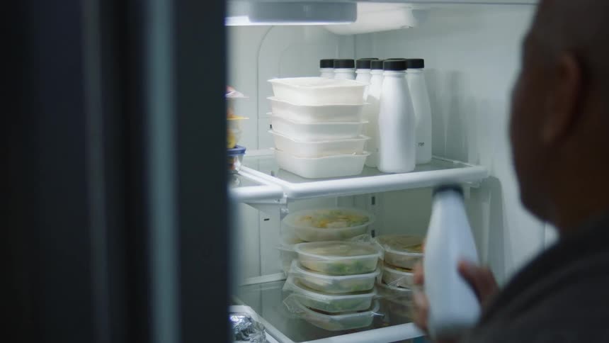 A person opens the doors of a fridge at home and takes a white bottle before closing them