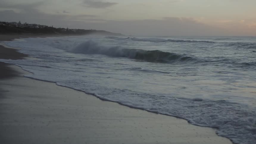Ocean waves washing ashore a sandy beach at sunset