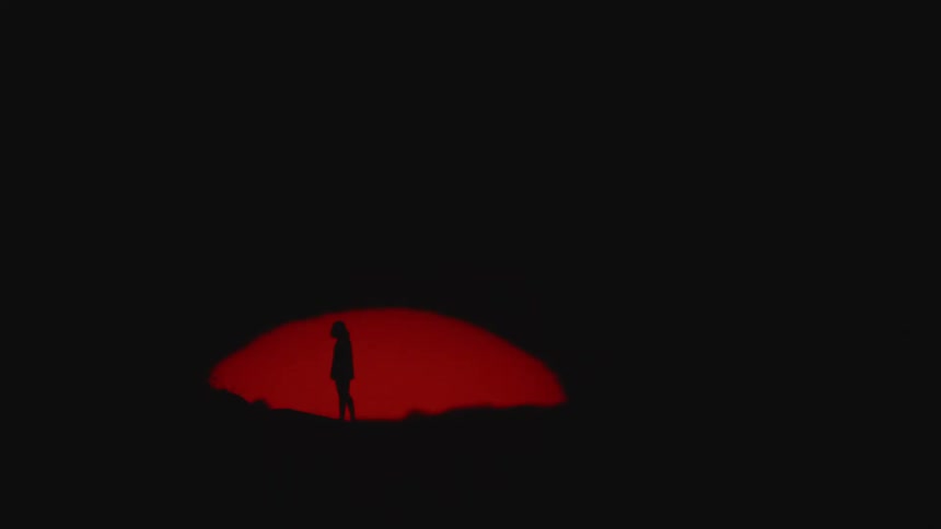 A silhouetted person standing in front of a setting red sun