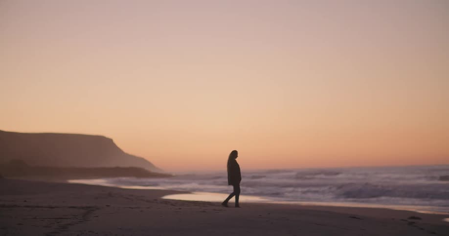 A silhouetted person walking alone on a beach at sunset