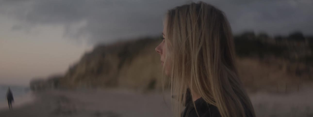 Close up of the face of a young woman standing on the beach looking at the horizon at evening