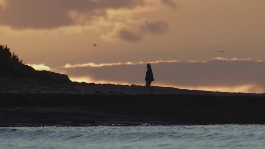 Silhouette of a woman climbing the gentle slope of a hill close to the coast at sunset