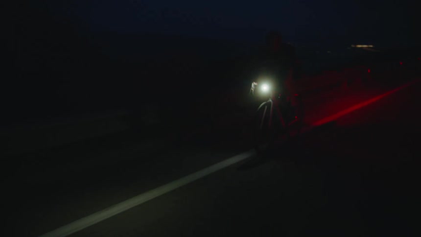 Woman wearing a crash helmet rides a bicycle on a road through the desert at night