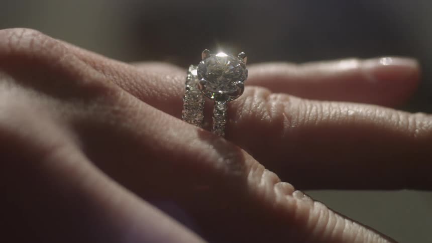 A large diamond ring is on a persons finger
