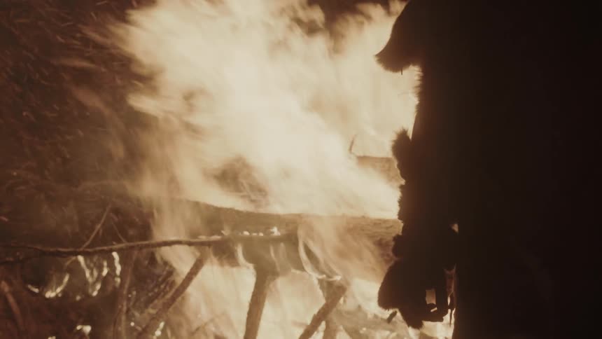 A person is standing by a large fire at night