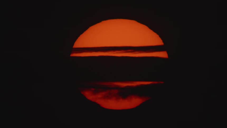 Giant red sun setting behind the clouds on a black sky at sunset