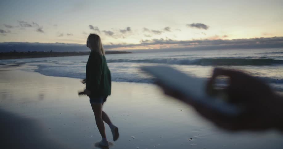 Two young girls dancing while walking on the beach with their phones at evening