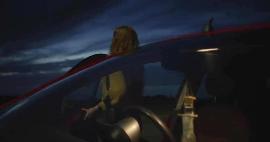 Two women are getting out of a parked car at the beach as the sun has set