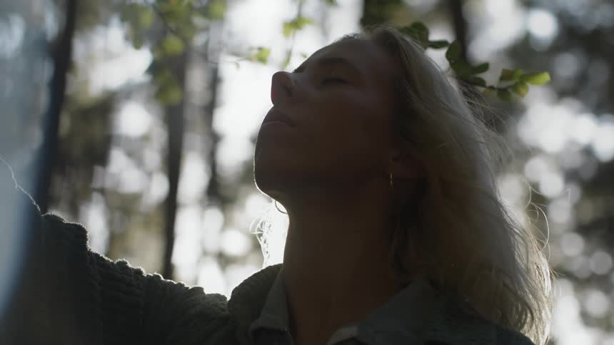 Close up of the face of a young woman looking at the tree branches on the forest at morning